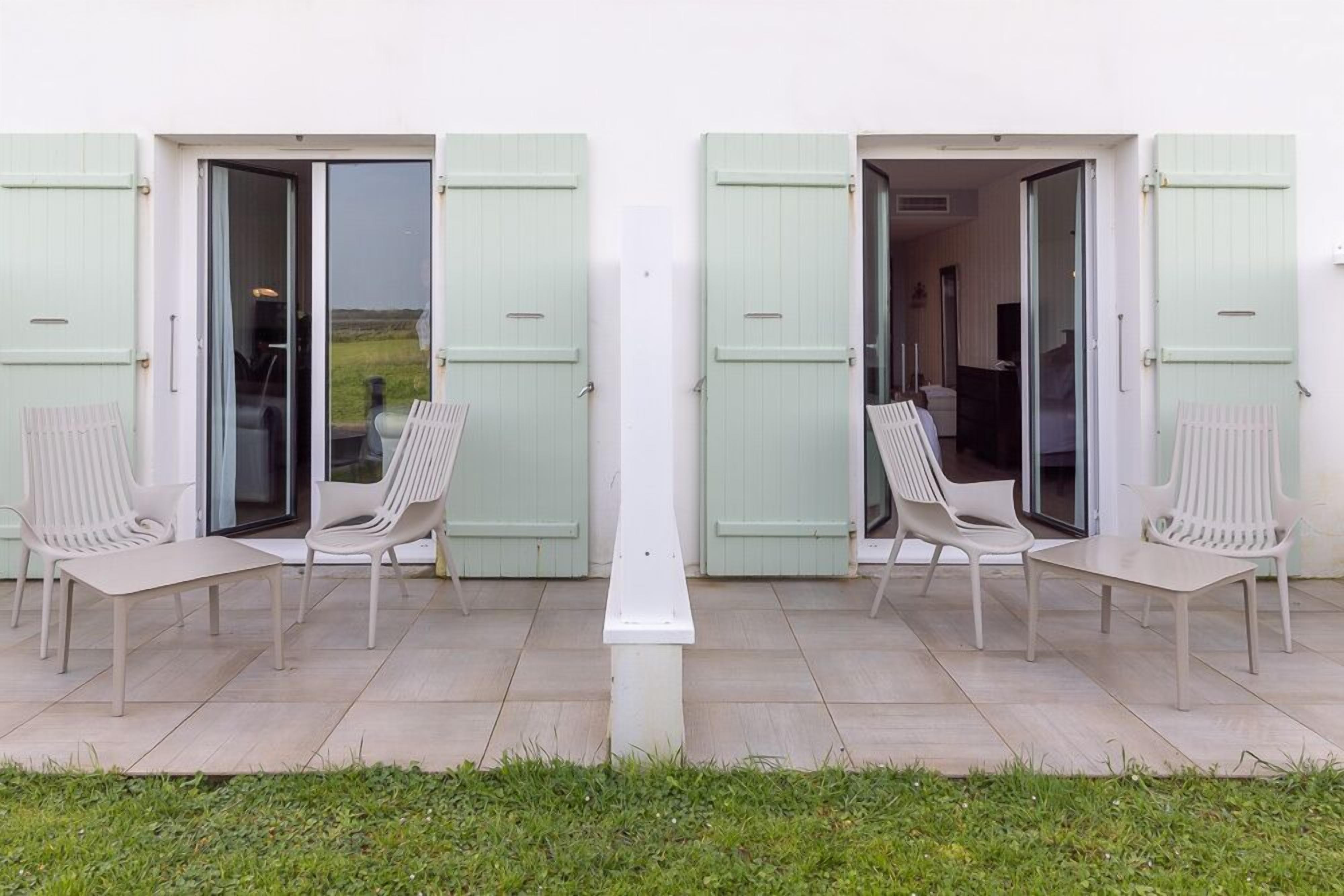 A patio with two open doors leading to a room, each with a pair of white chairs and a table.