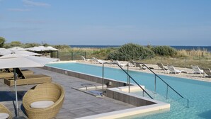 Ein Poolbereich mit Liegestühlen und Sonnenschirmen, mit freiem Blick auf das Meer und einer Holzterrasse.