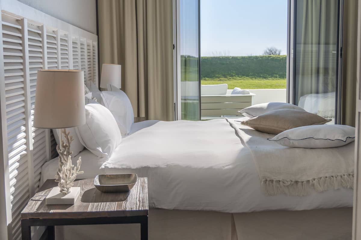 Une chambre à coucher avec un lit, une table de chevet, une lampe et une vue sur l’extérieur.