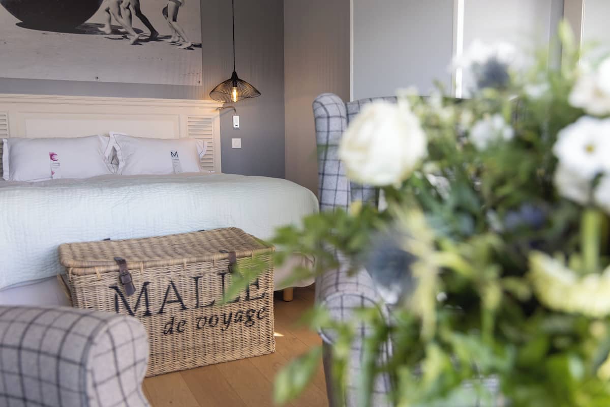 Une chambre à coucher avec un lit, une commode en osier, une chaise et une lampe fixée au mur.