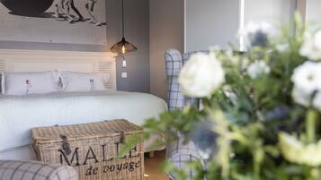 A bedroom with a bed, a wicker chest, a chair, and a wall-mounted lamp.