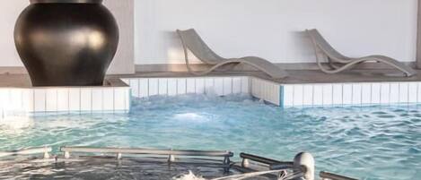 A modern indoor pool with clear water, lounge chairs, and a large black vase on the wall.