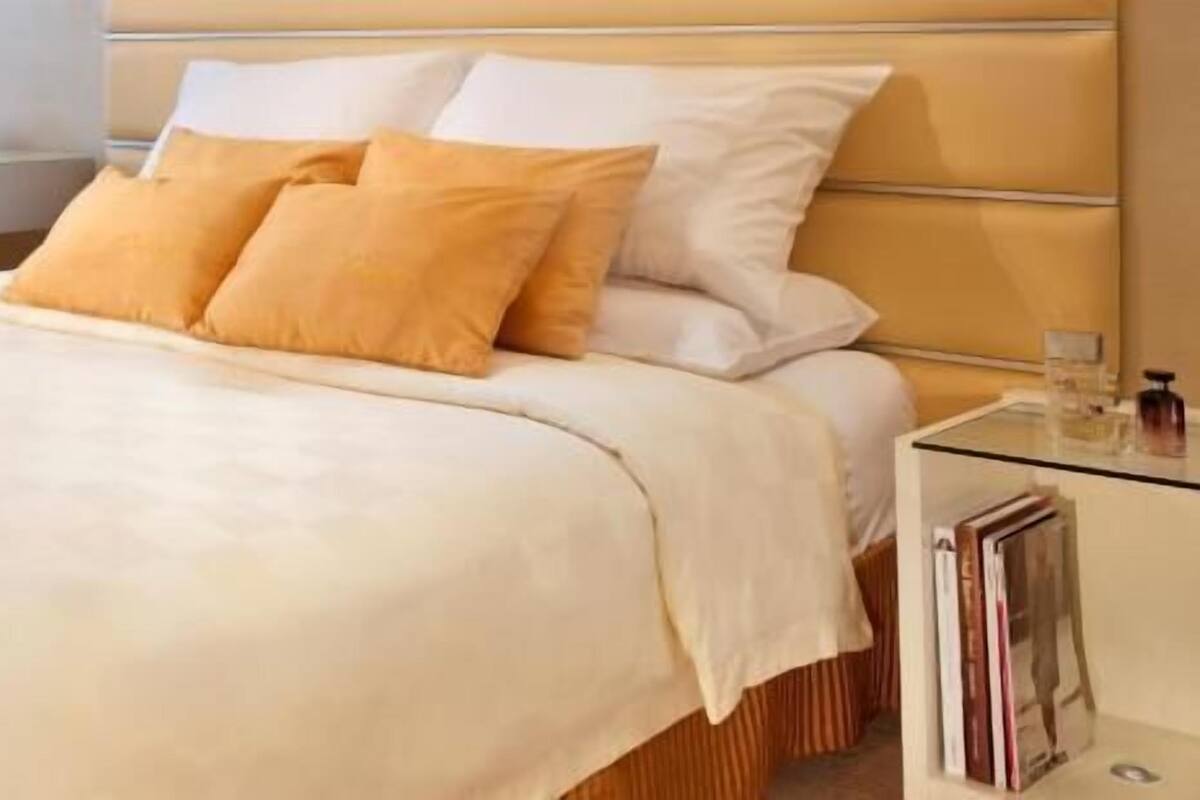 A bed with a beige headboard, white and yellow pillows, and a white bedspread.