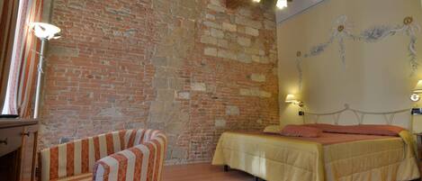 Una habitación con pared de ladrillo, una cama con cubrecama amarillo, un sillón a rayas y una araña.