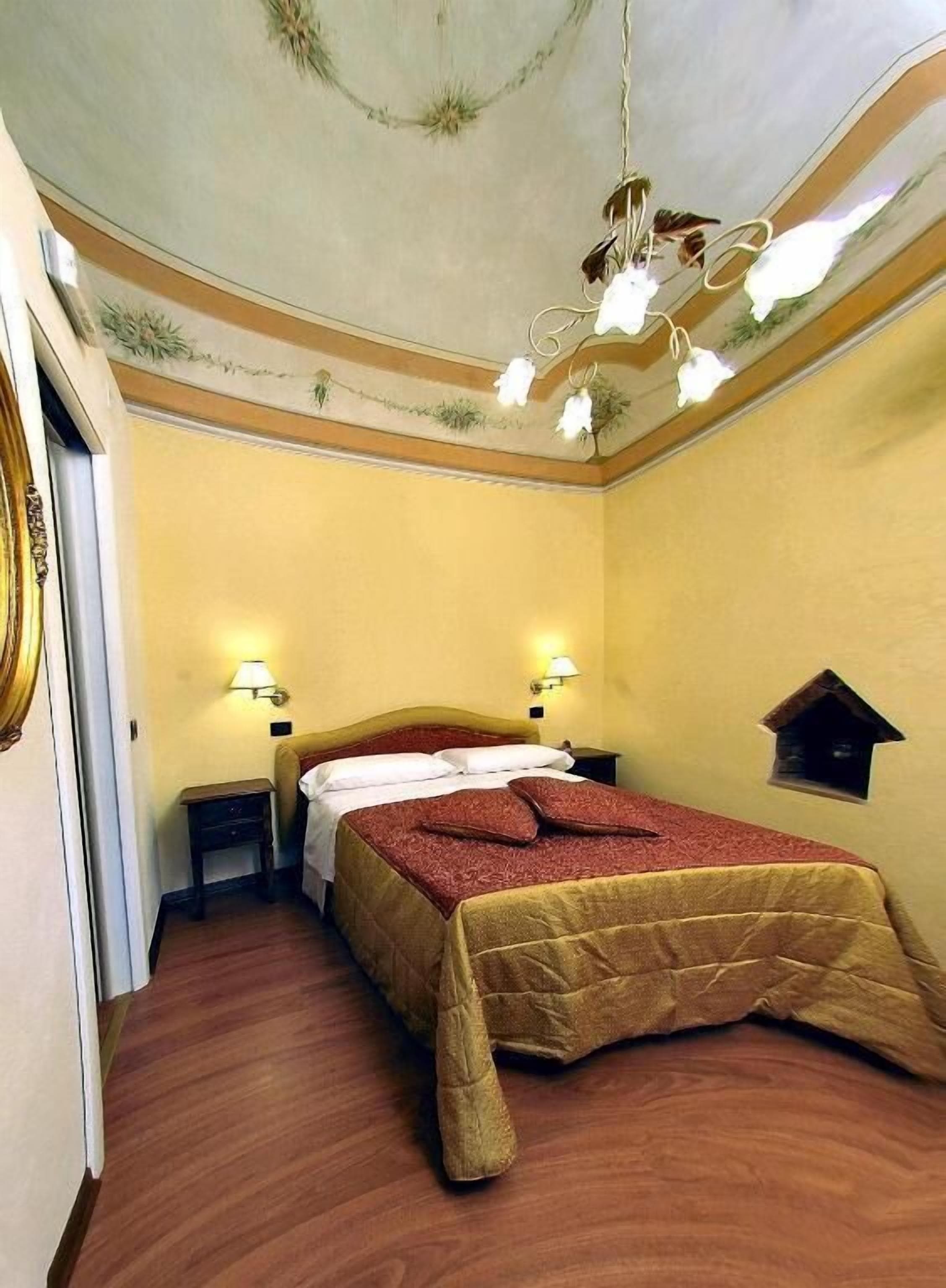 Una habitación de hotel con una cama, dos mesitas de noche, una araña y un pequeño adorno en la pared.