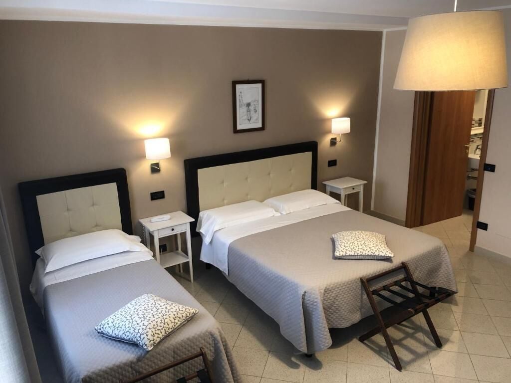 Ein Hotelzimmer mit zwei Betten, einem Nachttisch, einer Lampe und einem gerahmten Bild an der Wand.