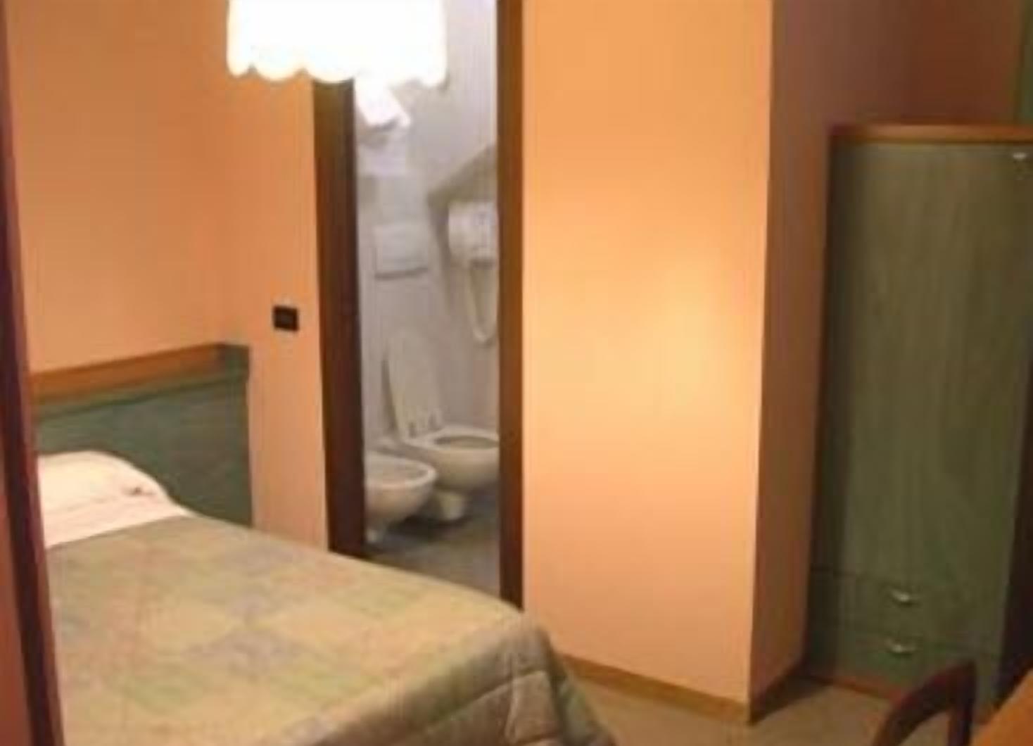 A small hotel room with a single bed, a wooden wardrobe, and a bathroom visible through an open door.