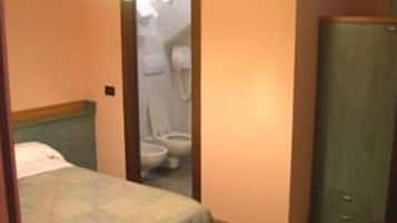 A small hotel room with a single bed, a wooden wardrobe, and a bathroom visible through an open door.