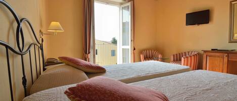 A hotel room with two beds, a television, a lamp, and a view of the outside.