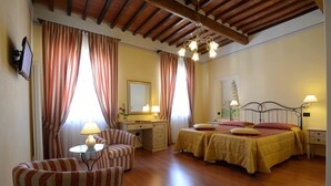 Quarto de hotel com teto de madeira, cama com roupa de cama amarela, escrivaninha com luminária, uma cadeira e um espelho na parede.