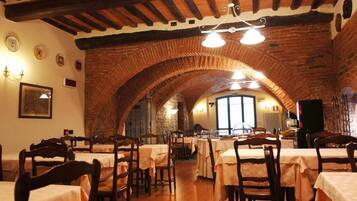 Un ristorante con archi in mattoni, travi in legno e tavoli apparecchiati con tovaglie bianche.