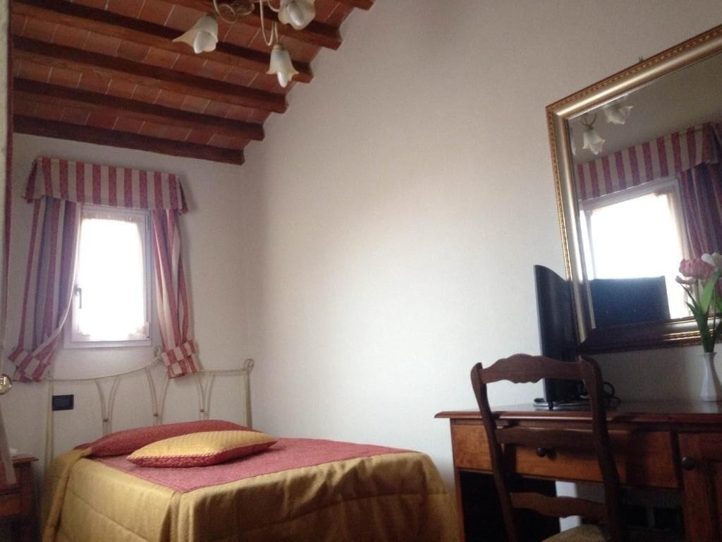 Un dormitorio con cama, escritorio, silla, espejo y ventana con cortinas.