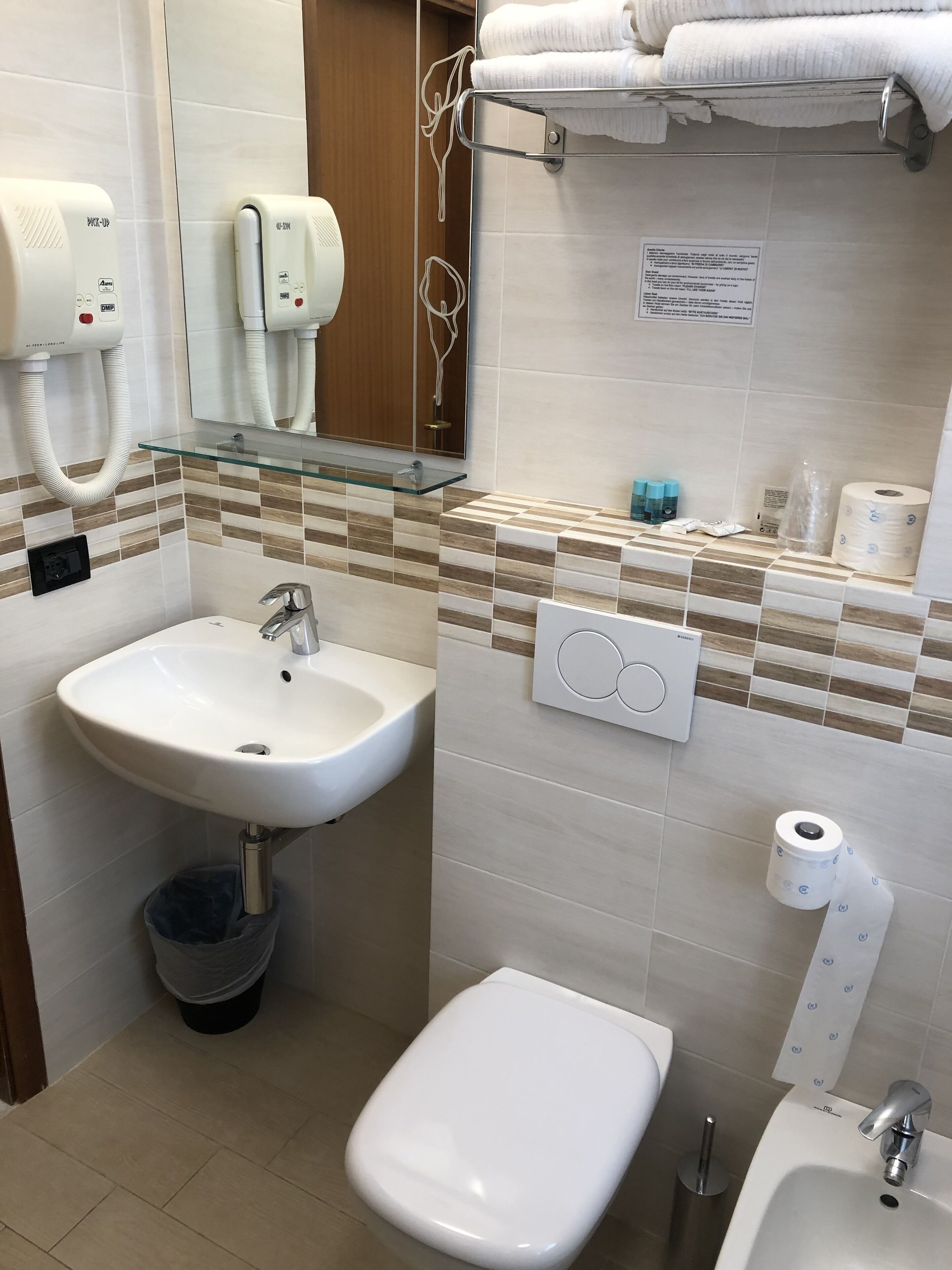 Un baño moderno con repisa de vidrio, lavamanos blanco, un bidé y un inodoro.
