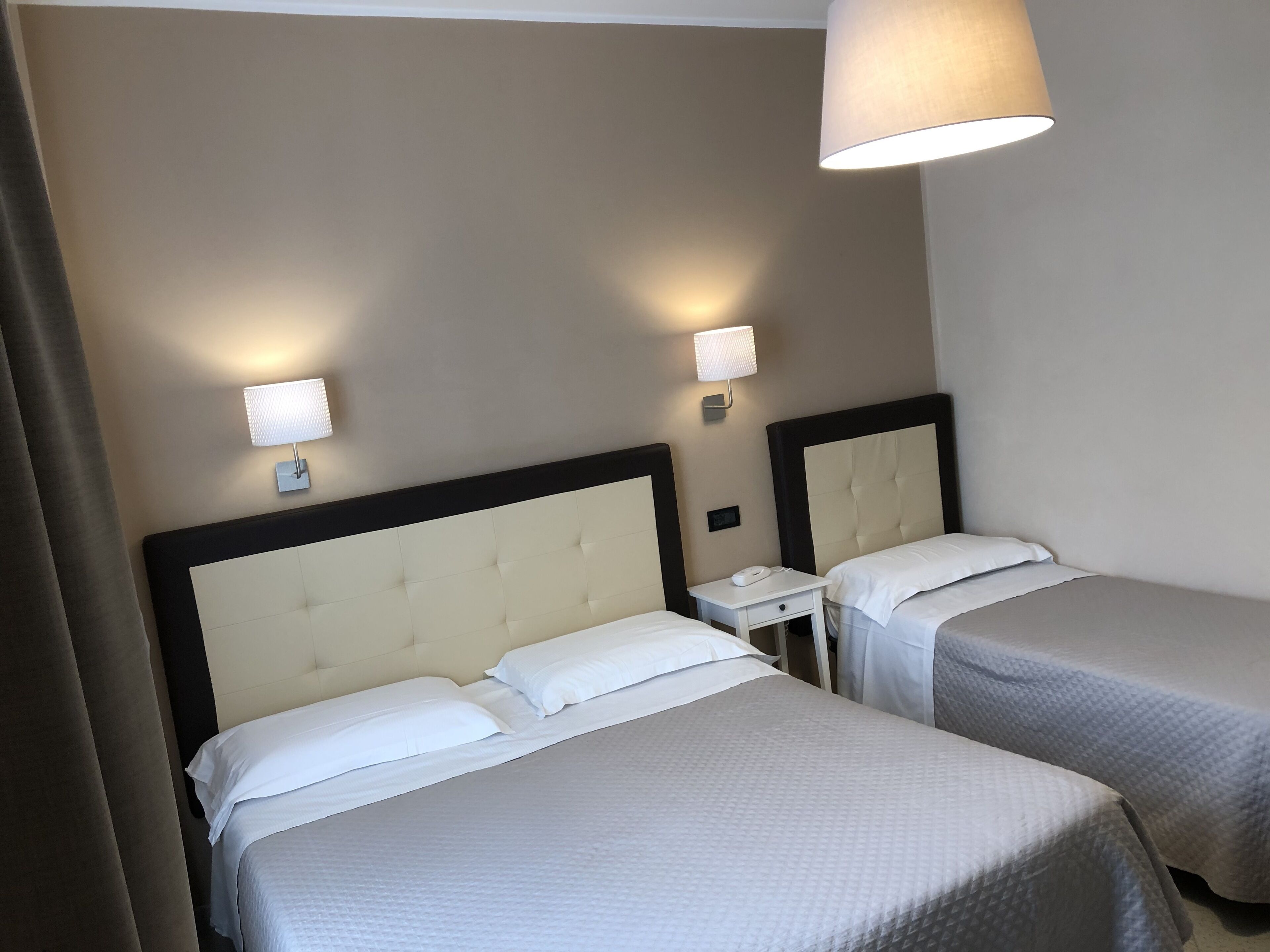 Habitación de hotel con dos camas, cada una con cabecero y mesita de noche. Hay lámparas de pared a cada lado de las camas.