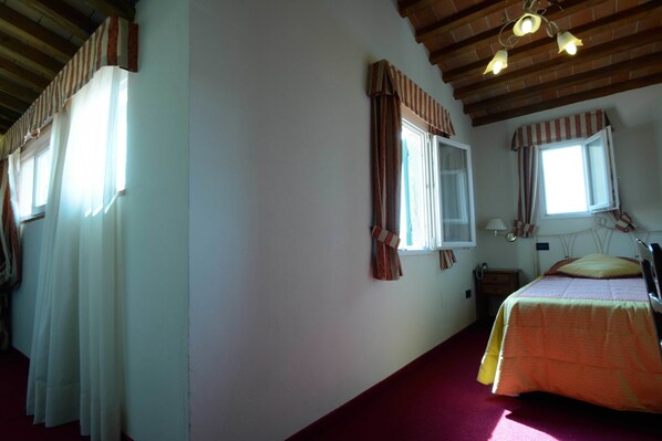 Un dormitorio con una cama, una mesita de noche, un ventanal con cortinas y techo de madera.