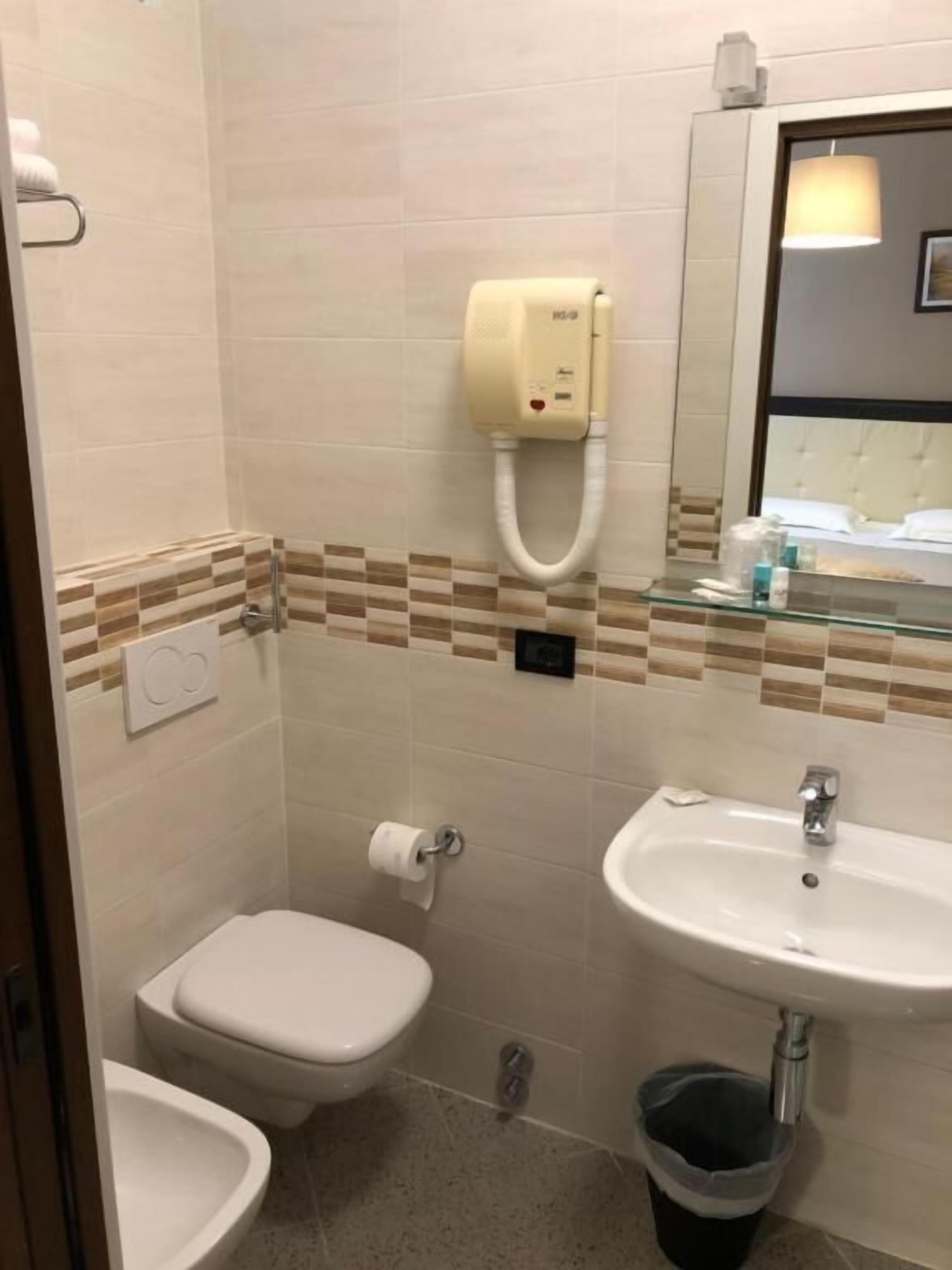 A bathroom with a toilet, bidet, sink, and hand dryer.