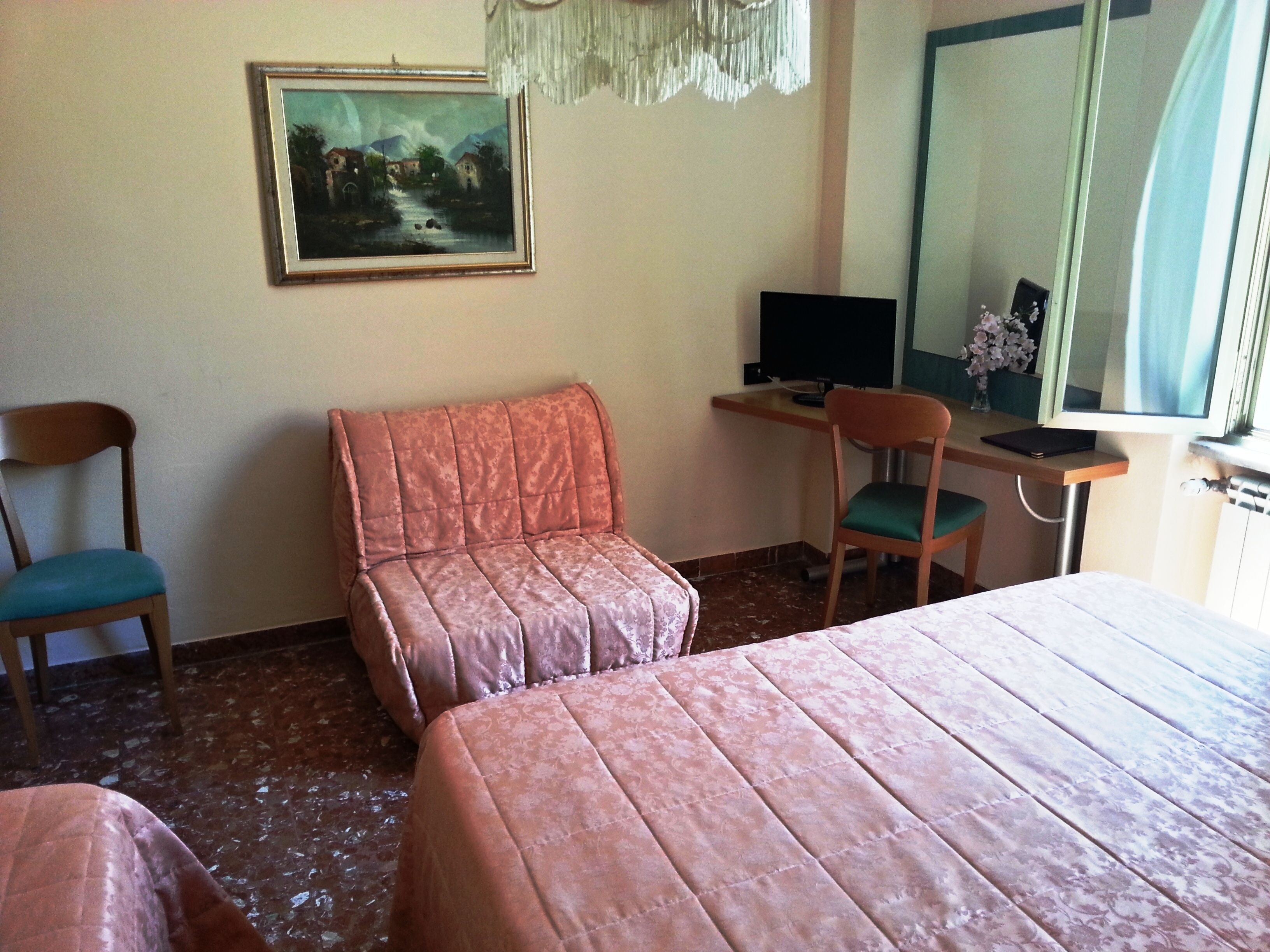 Habitación de hotel con dos camas, un escritorio con computadora, una silla y un cuadro en la pared.