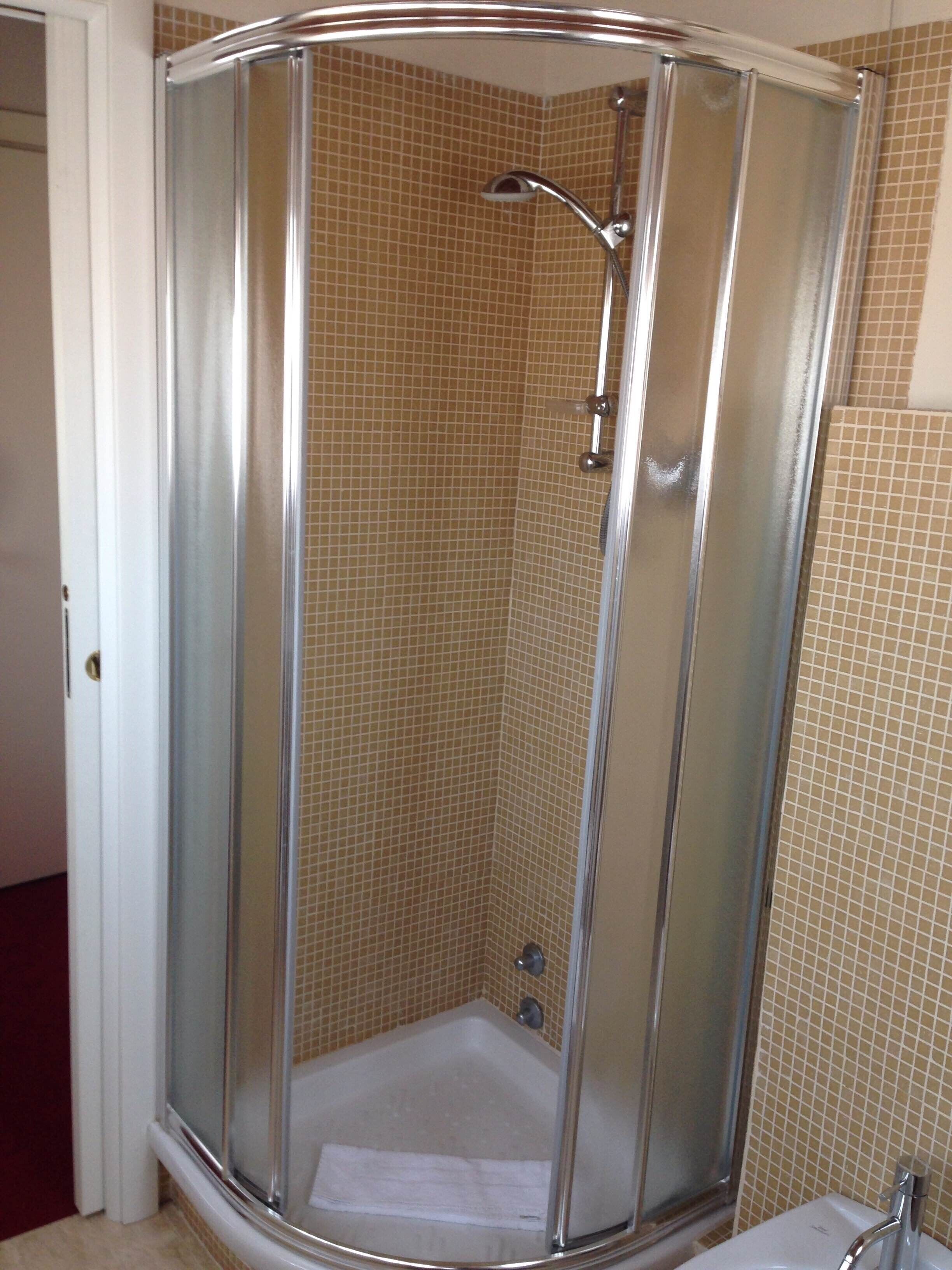 A glass-enclosed shower stall with a tiled floor and a white bathtub.