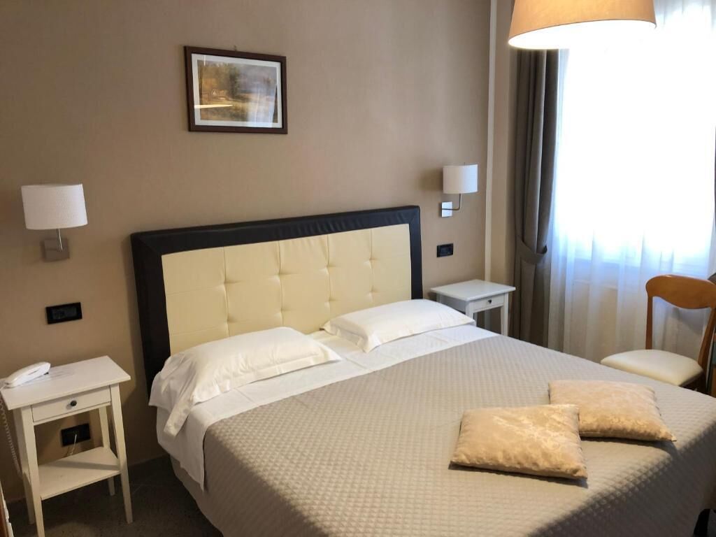 Una habitación de hotel con una cama grande, dos mesitas de noche, una silla y una lámpara.