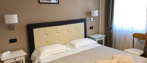 Una habitación de hotel con una cama grande, dos mesitas de noche, una silla y una lámpara.