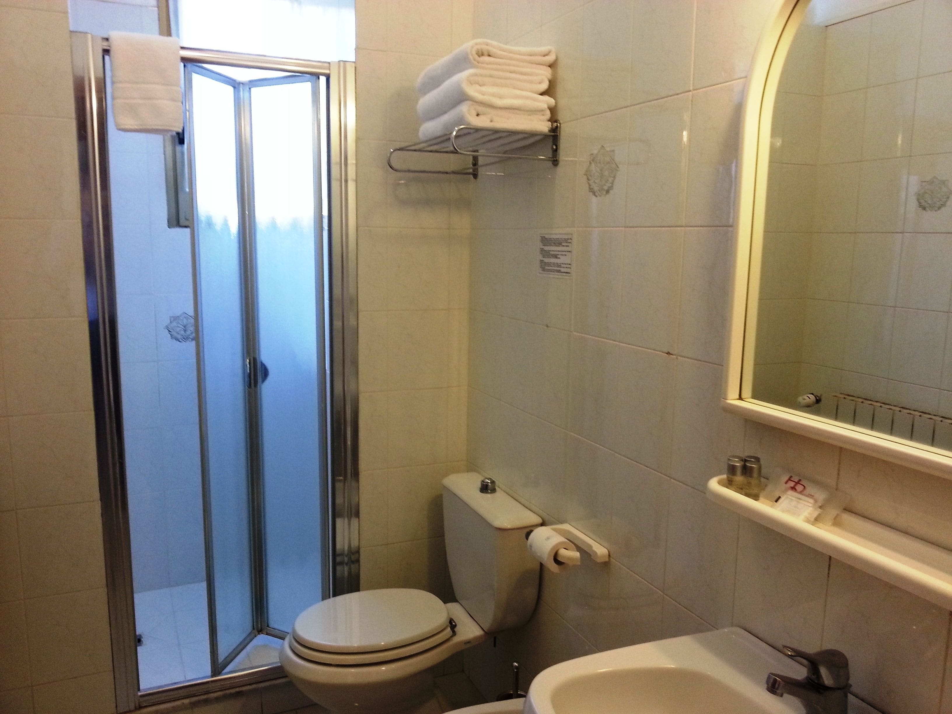 A bathroom with a glass shower door, a toilet, a sink, and a towel rack.