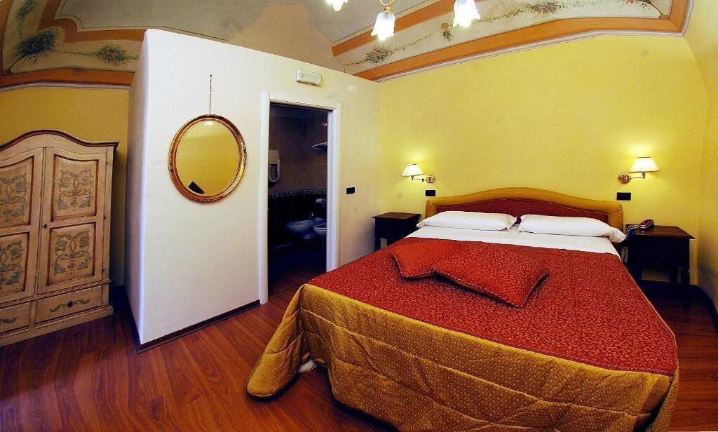 A hotel room with a bed, a wardrobe, a mirror, and a door leading to a bathroom.
