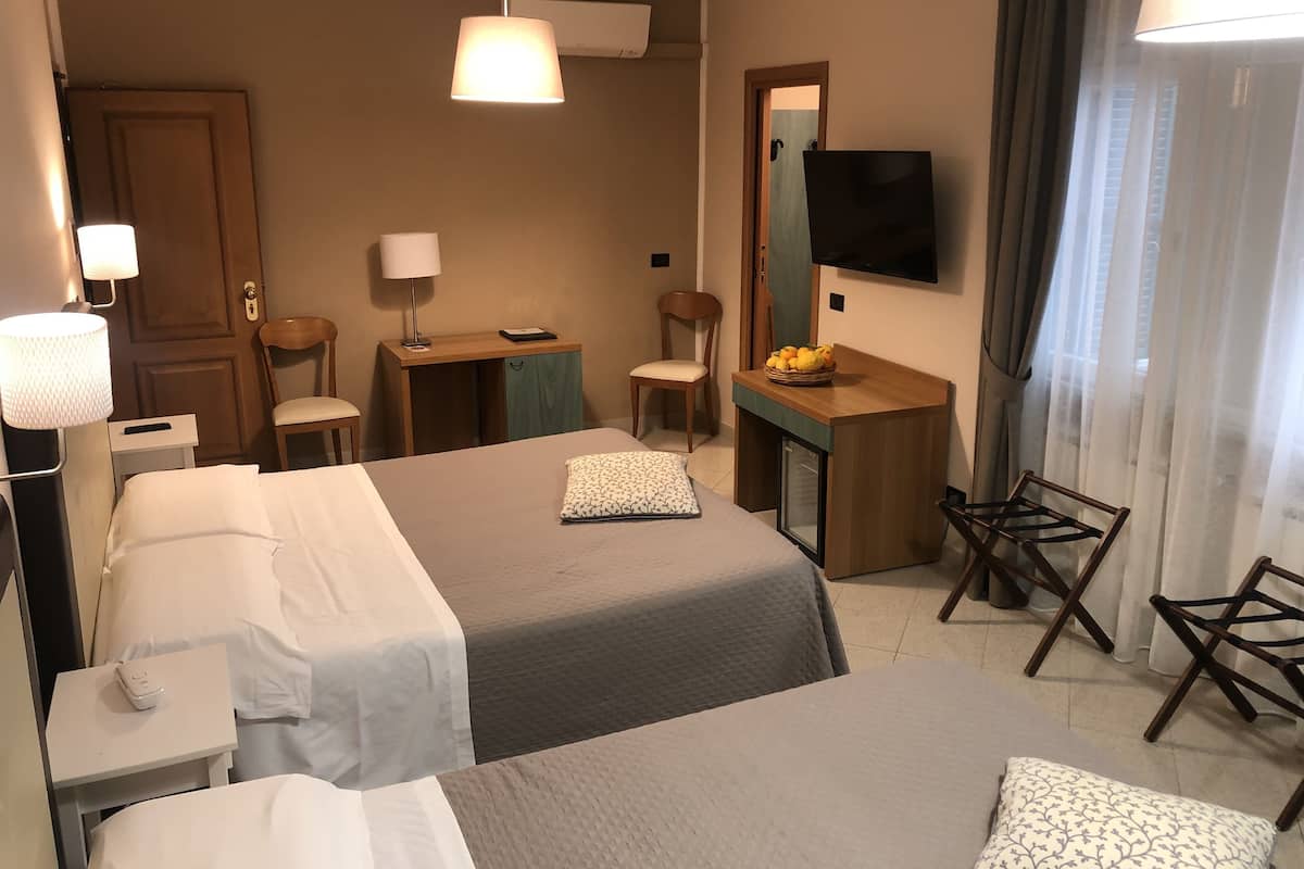 Habitación de hotel con dos camas, un escritorio, una silla, un televisor y una mesita con fruta.
