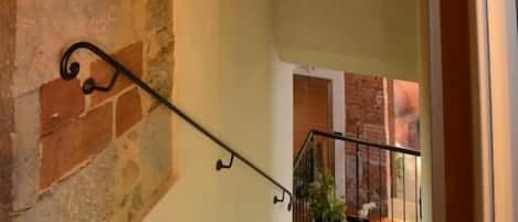 Una escalera con un muro de ladrillo a un lado y una pared lisa al otro, que desciende a un nivel inferior.