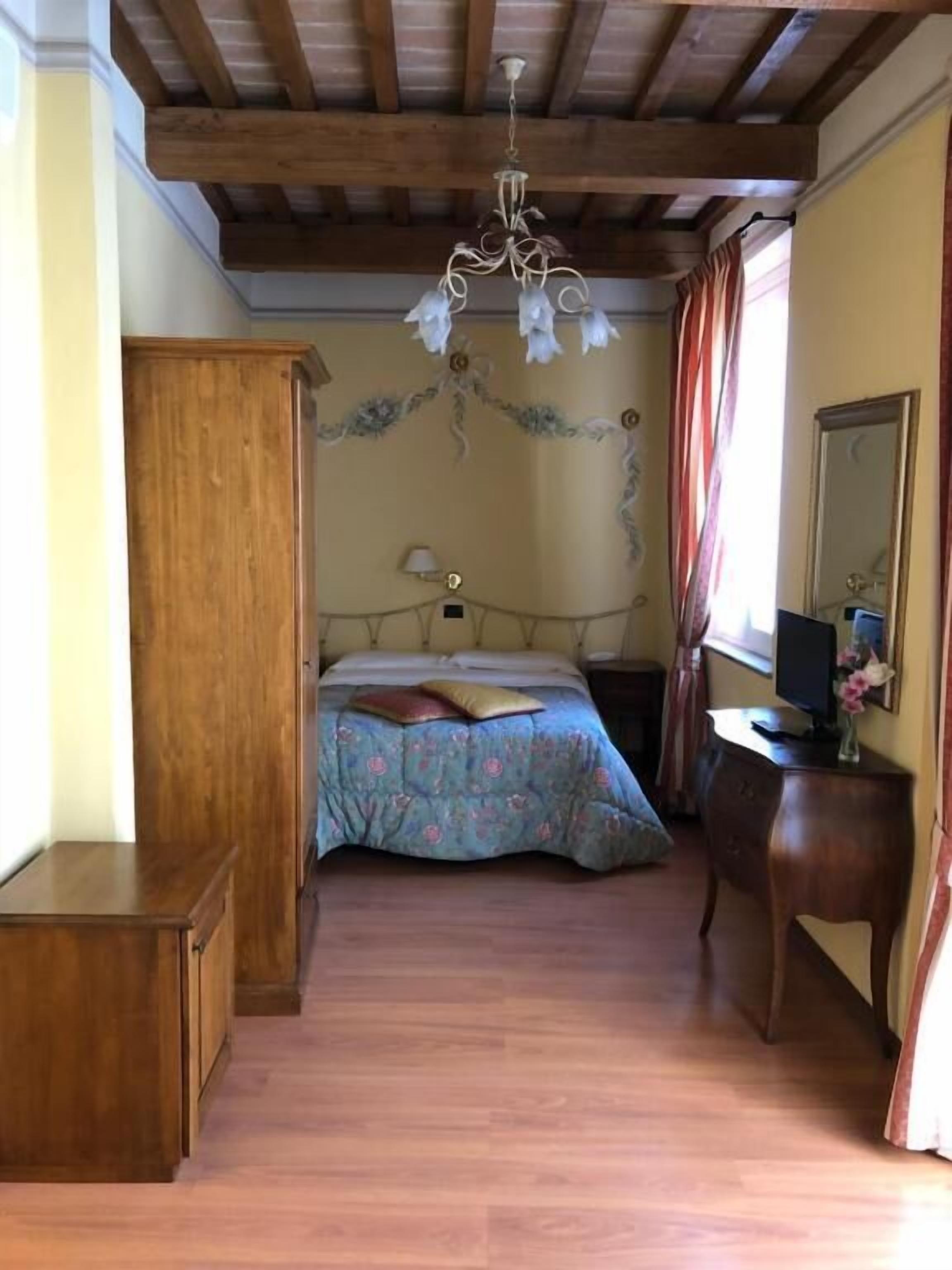 A bedroom with a wooden ceiling, a bed with floral bedding, a bedside table, a dresser, and a mirror.