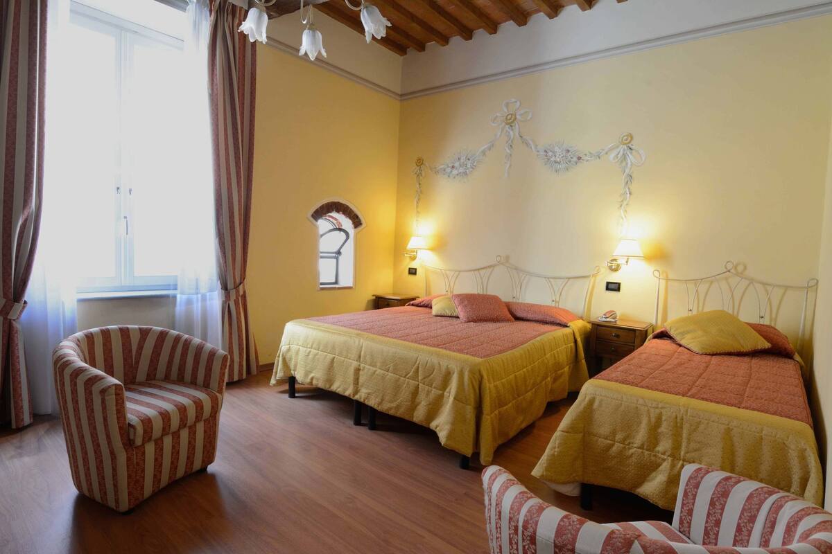 Habitación de hotel con dos camas, un sillón a rayas y un ventanal con cortinas.