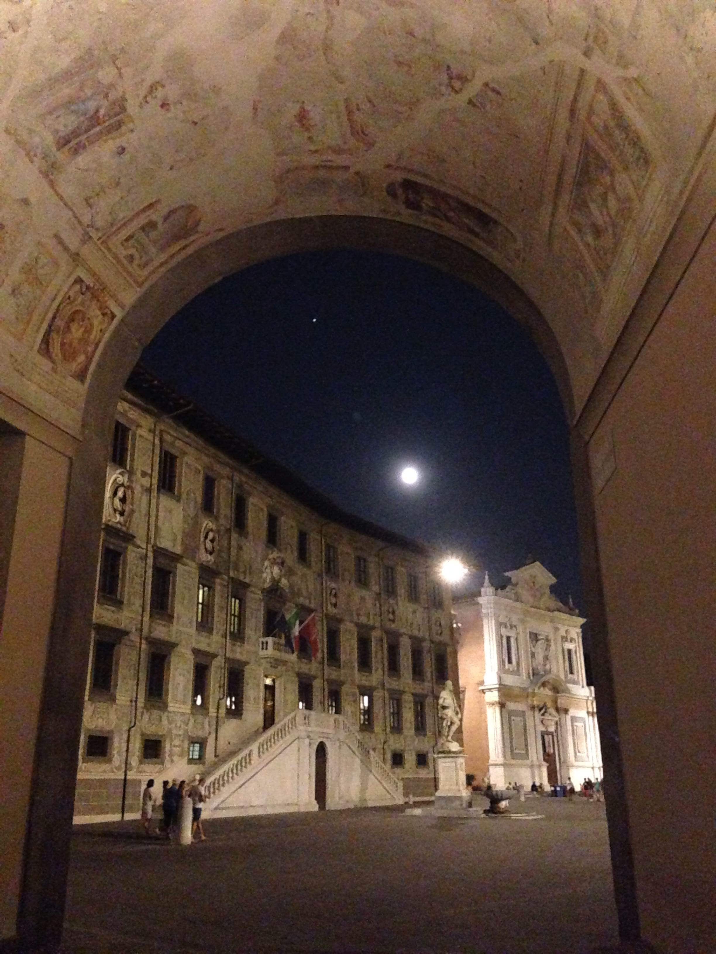Una entrada arqueada con fachada de edificio de arquitectura clásica y la luna en el cielo.