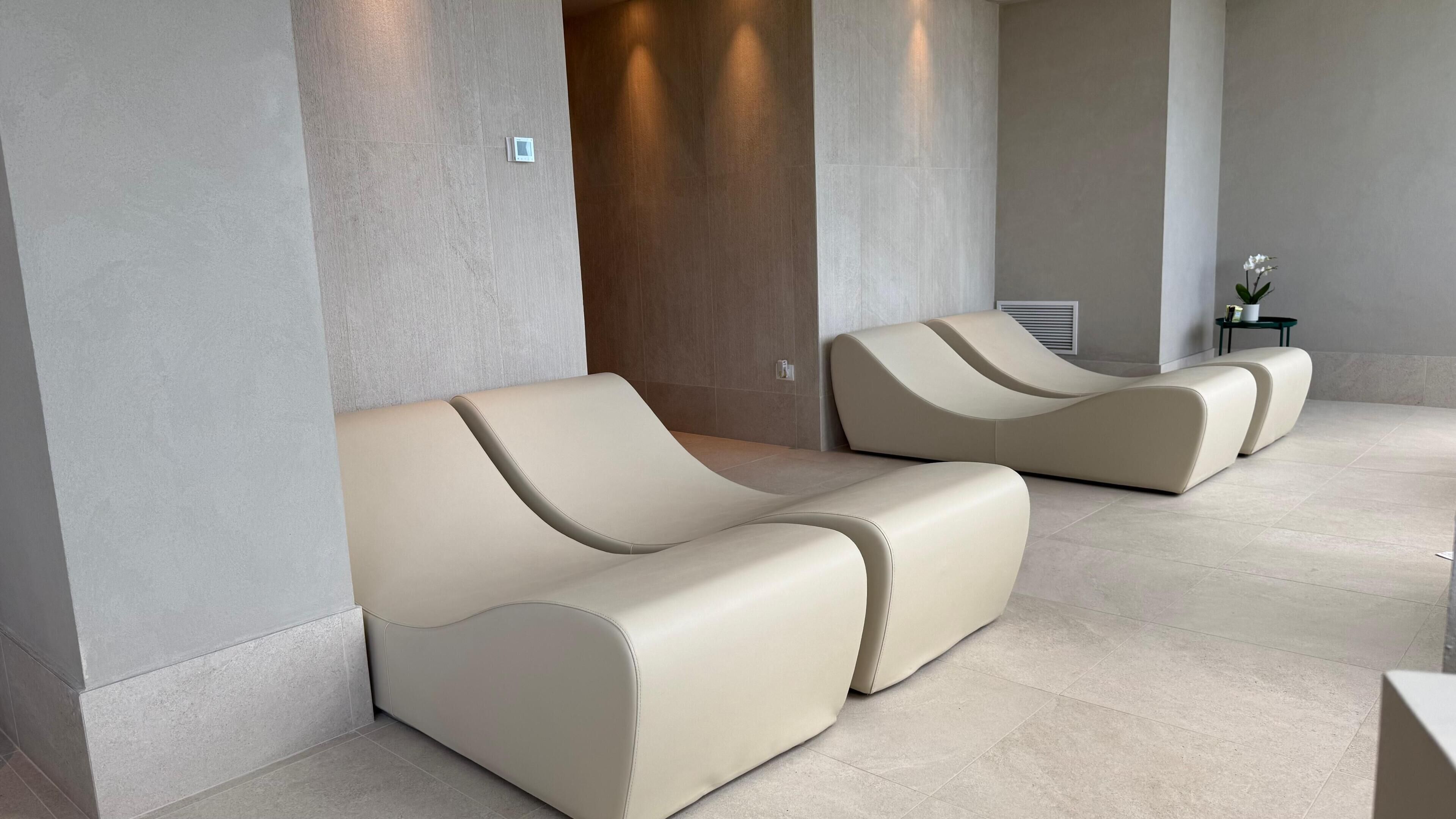 A modern waiting area with two beige sofas, a small table with a potted plant, and a wall-mounted air vent.