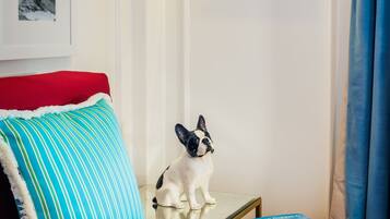 Un dormitorio ordenado con una cama roja, un almohadón a rayas, una mesita con una figurita de perro y cuadros en la pared.