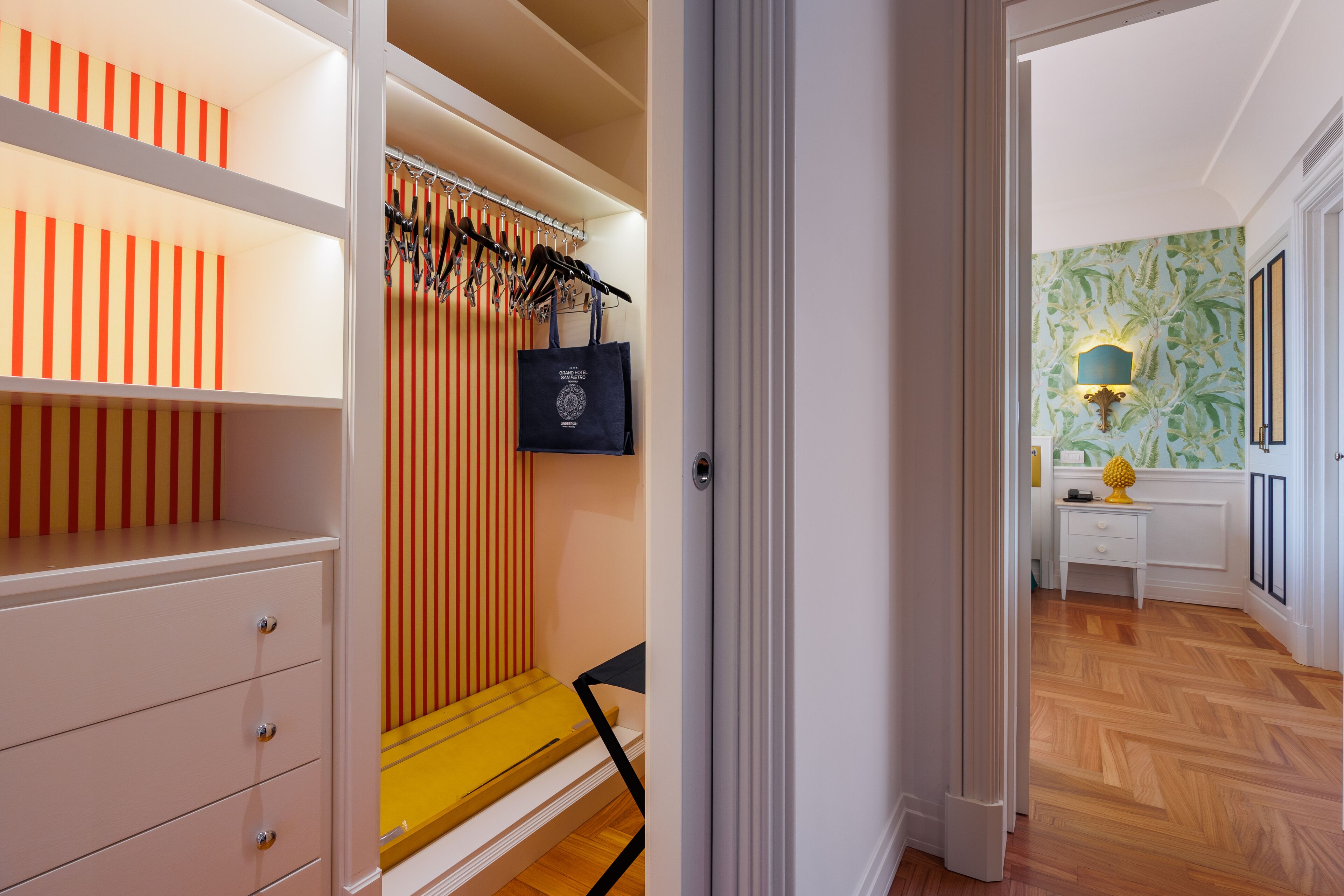 A hallway with a wooden floor, a white desk with a lamp, and a wall with a leafy pattern.