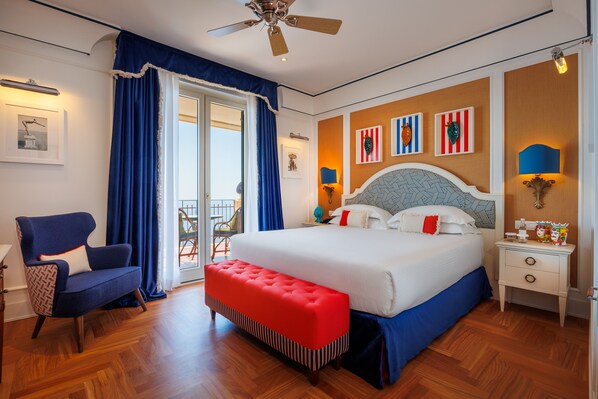 Un dormitorio con una cama grande, una silla, un banco, un ventilador de techo y obras de arte en las paredes.