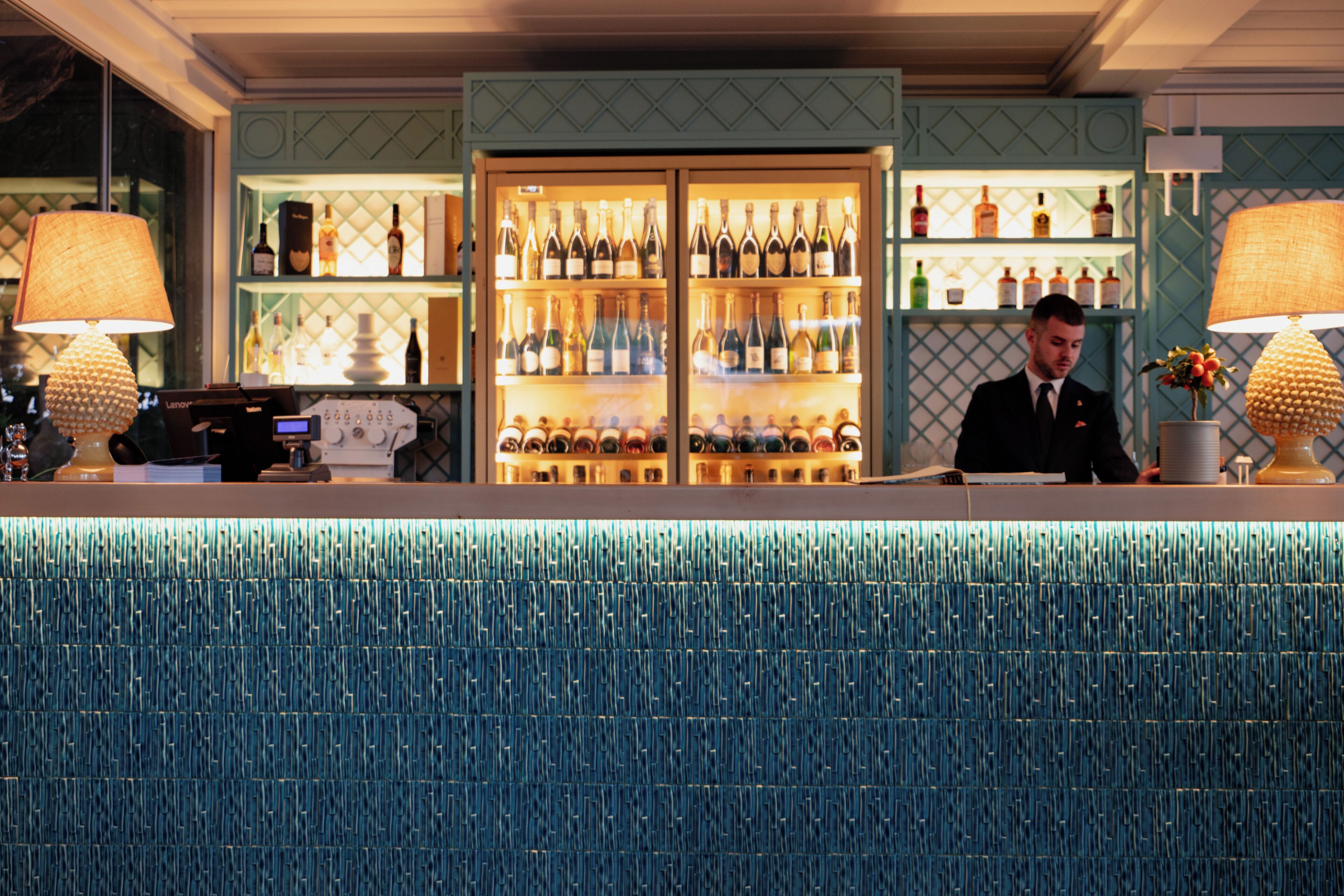 A bar area with a bartender, a wine cooler, and a patterned blue wall.