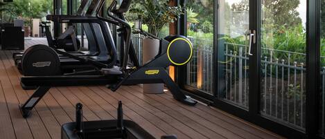 A gym with exercise equipment, large windows, and a wooden deck.