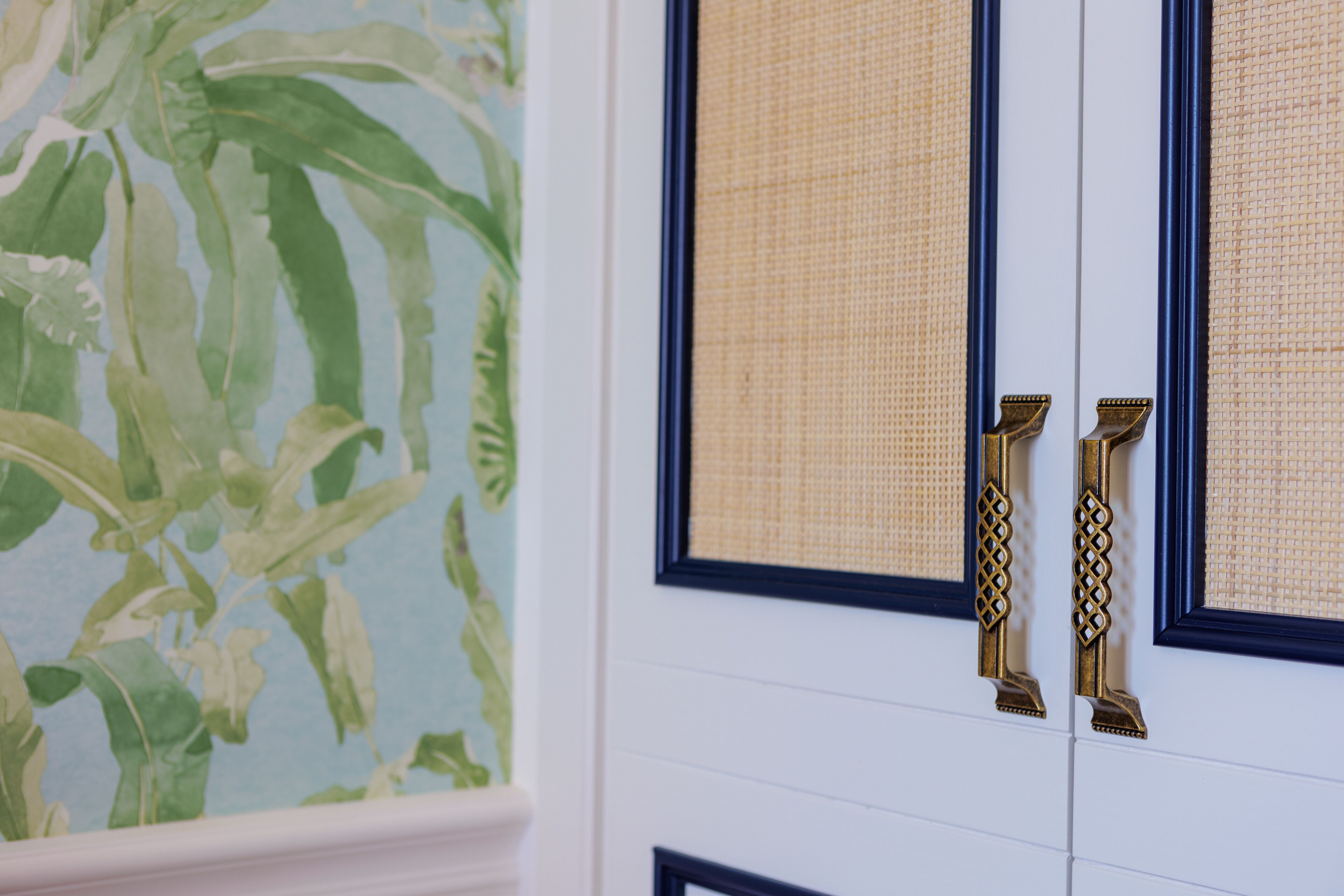 A door with a woven mat and brass handles, adjacent to a wall with a green leafy wallpaper.