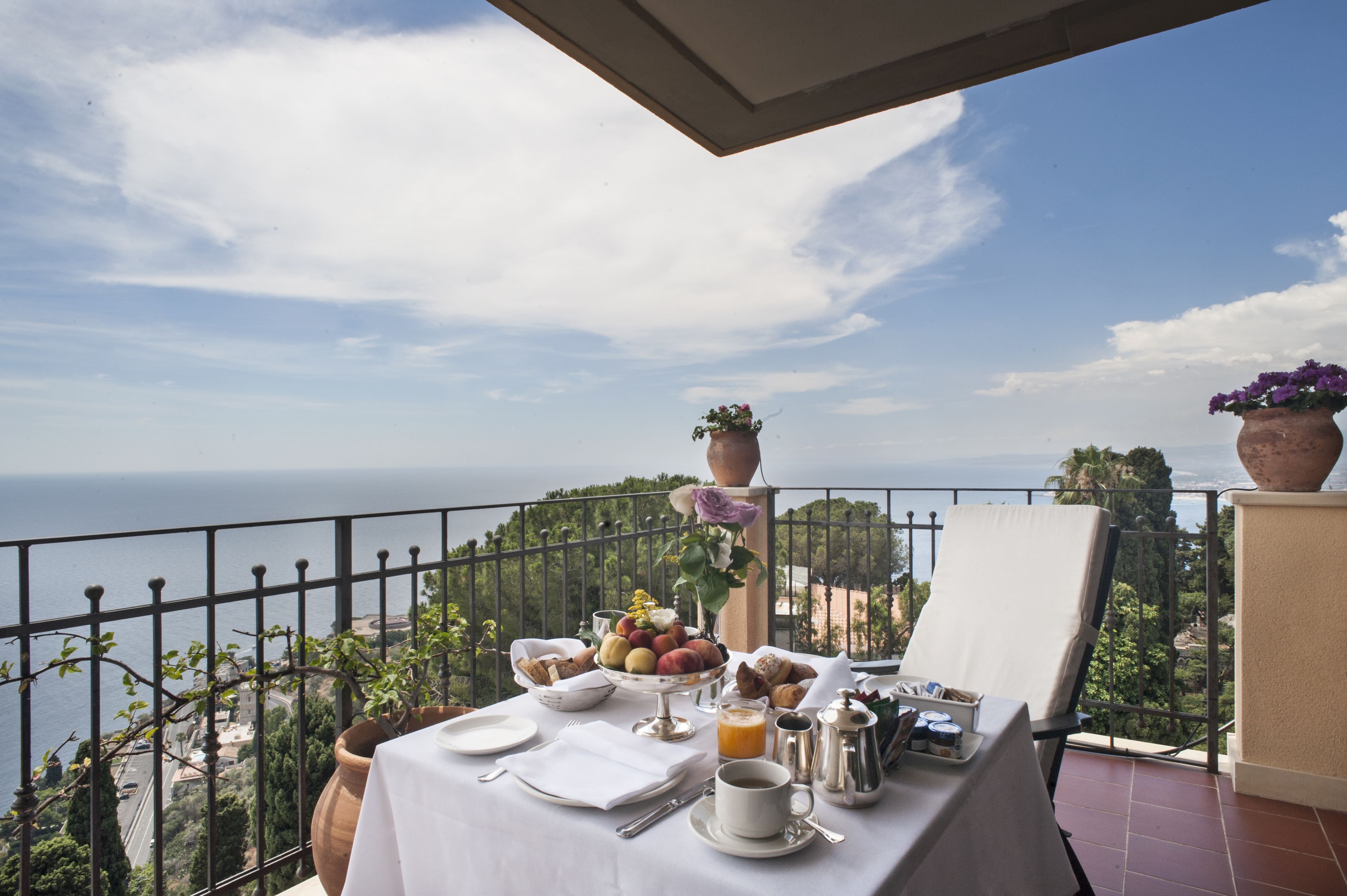 A balcony with a table set for breakfast, overlooking a scenic view of the sea and greenery.