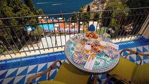 Un balcón con una mesa dispuesta para el desayuno, con vista a una piscina y al mar.