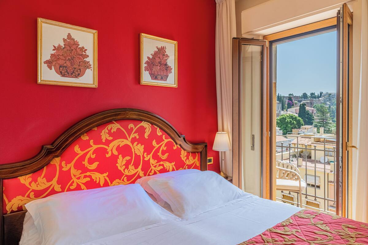 A hotel room with a red wall, a bed with white bedding, and two framed floral pictures.