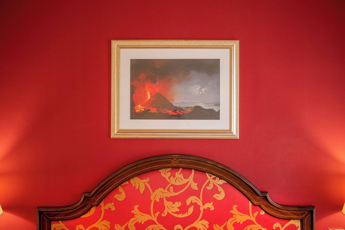 A framed picture of a volcanic eruption on a red wall.