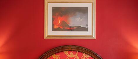 A framed picture of a volcanic eruption on a red wall.