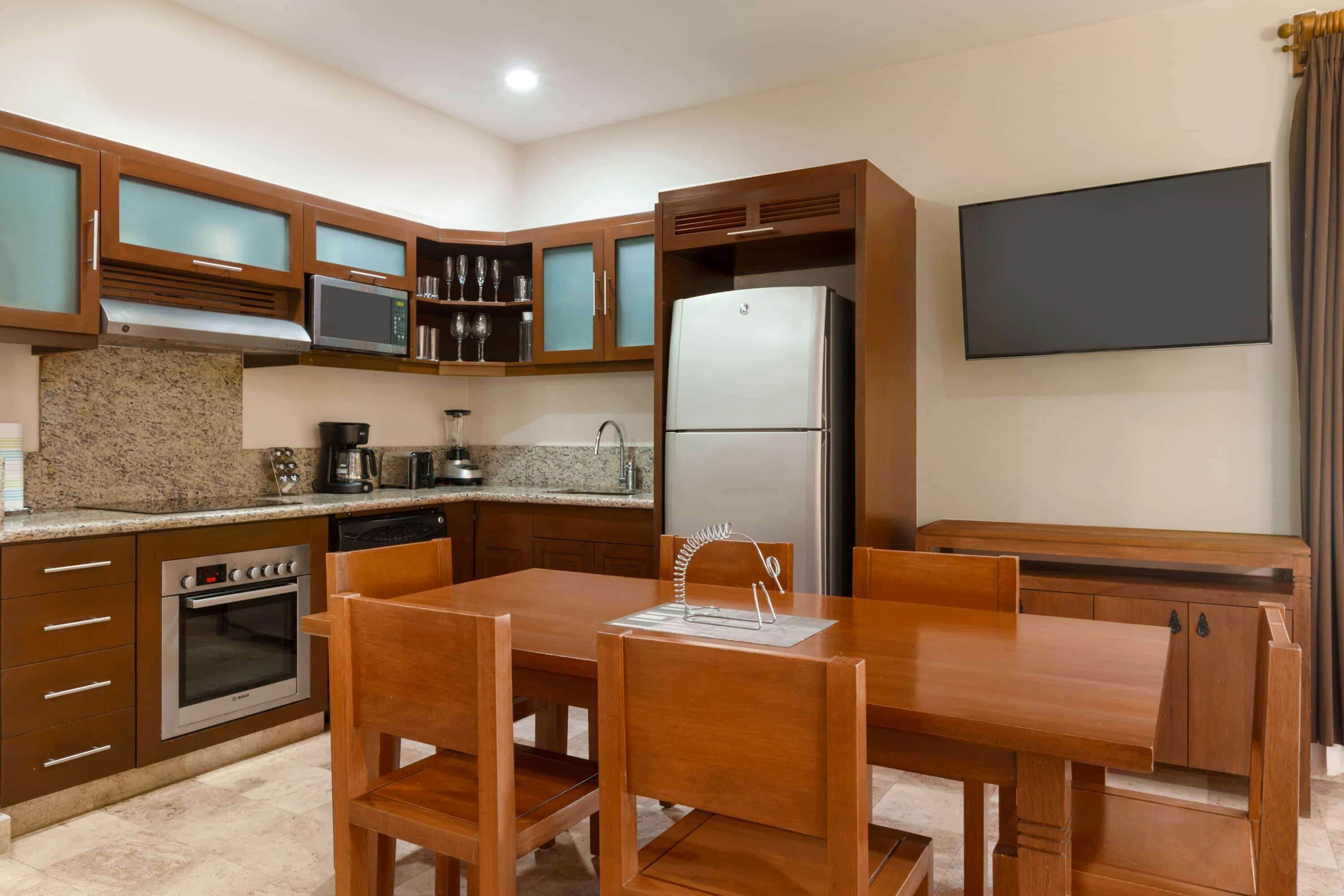 A modern kitchen with granite countertops, stainless steel appliances, wooden cabinets, and a dining area with a table and chairs.
