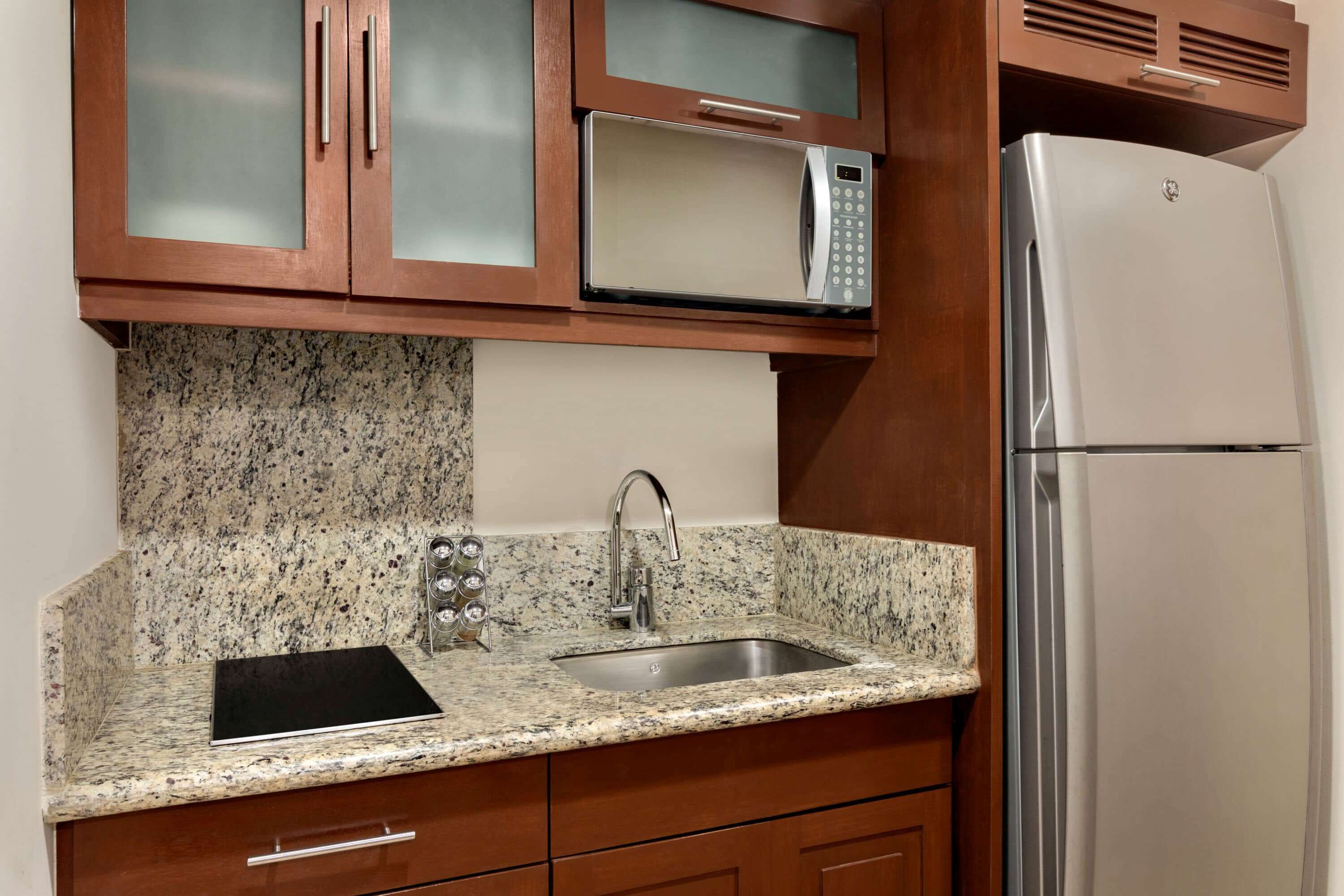 A kitchen with granite countertops, a stainless steel sink, a microwave, and a refrigerator.