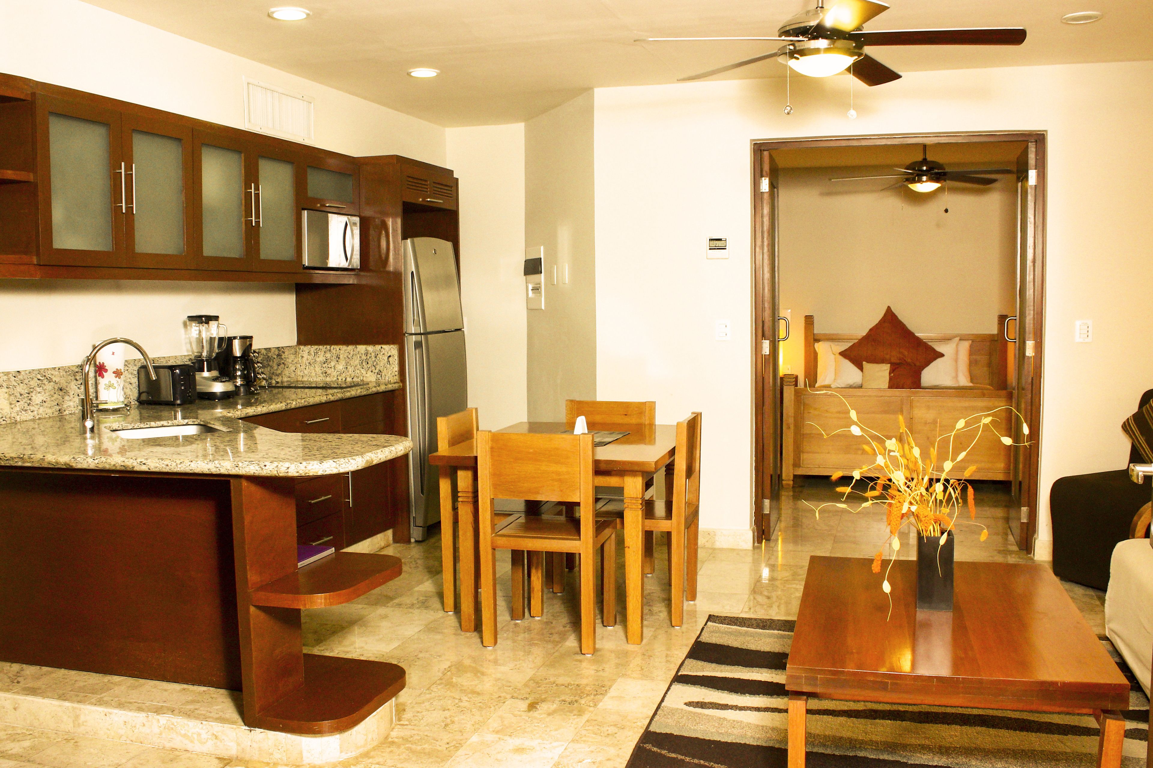 Una cocina moderna con encimeras de granito, armarios de madera, un refrigerador y un comedor con mesa y sillas.