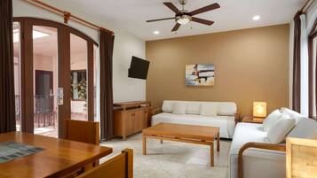 A modern living room with a sofa, coffee table, and wooden furniture. A ceiling fan and TV are mounted on the wall.