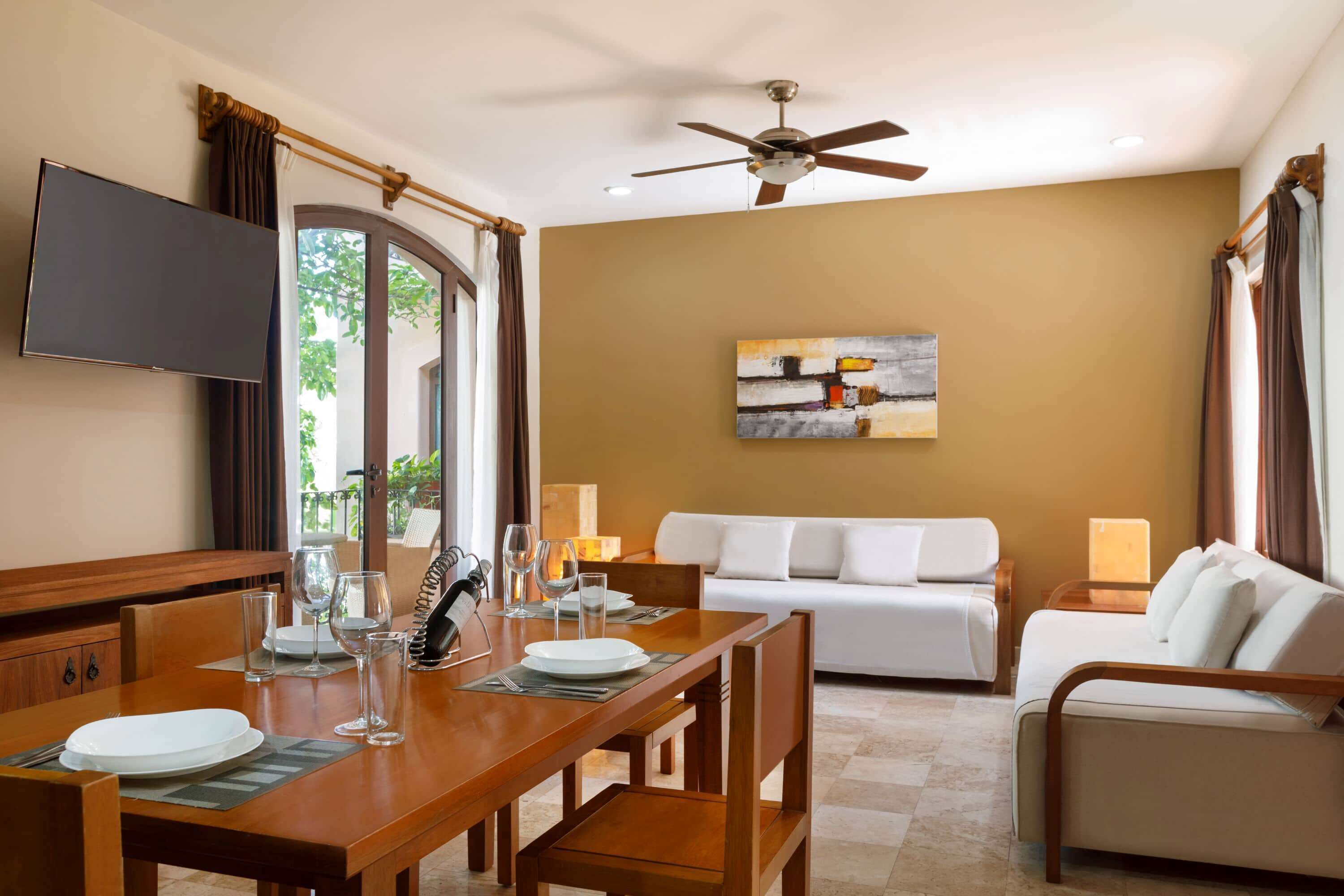 A well-lit room with a dining table set for two, a white sofa, and a ceiling fan.