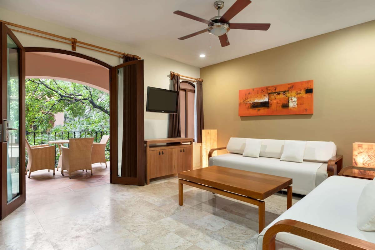 Una habitación de hotel moderna con balcón, un sofá, una mesa de centro y un televisor.