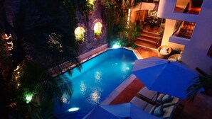 Una piscina con un arco de piedra, rodeada de palmeras y una escalera que lleva a un nivel superior.